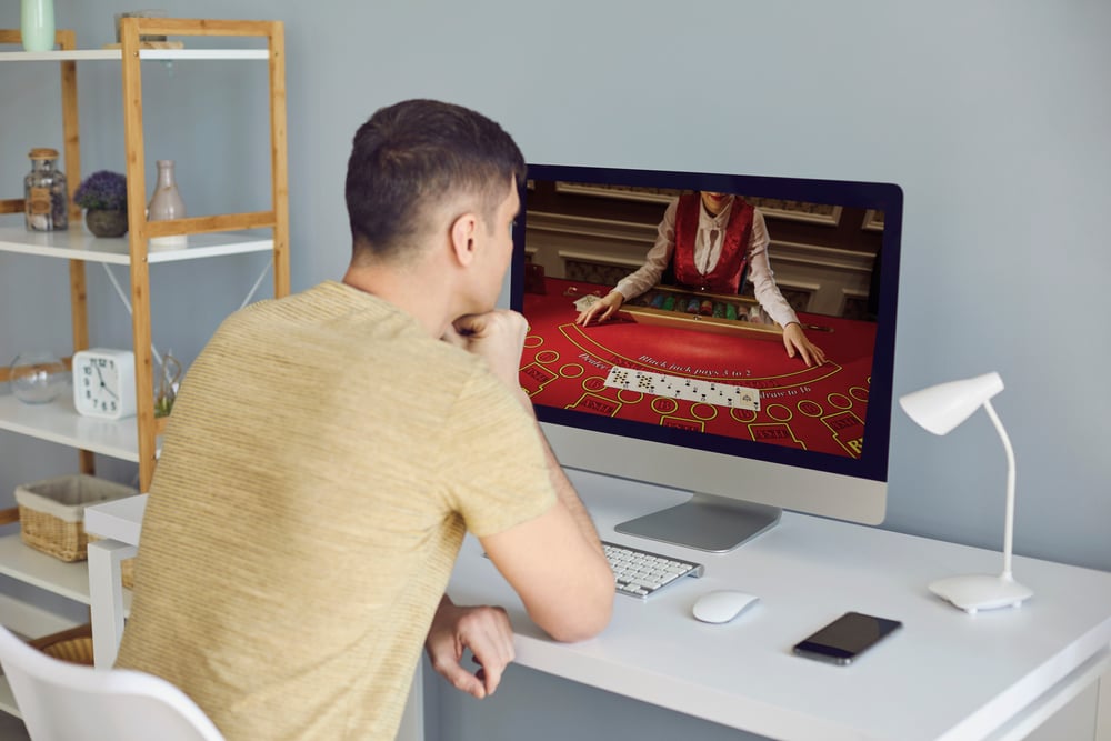 man sits at desk to watch a live dealer casino game on his desktop computer