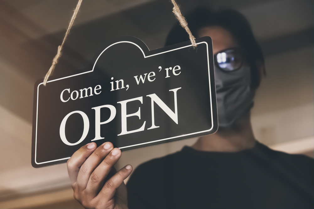 Masked person turning a store sign to indicate that it is open