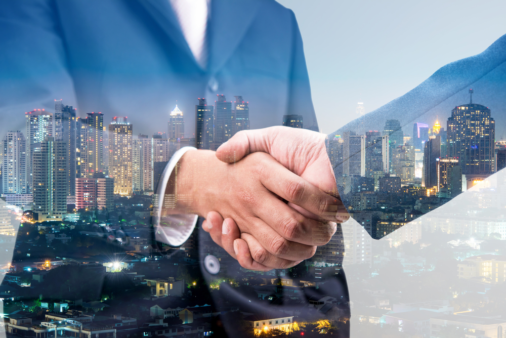 two businessmen shaking hands against a city nighttime backdrop