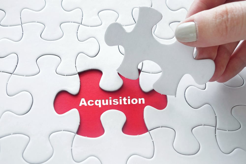 female's hand places last jigsaw puzzle piece to cover the word acquisition