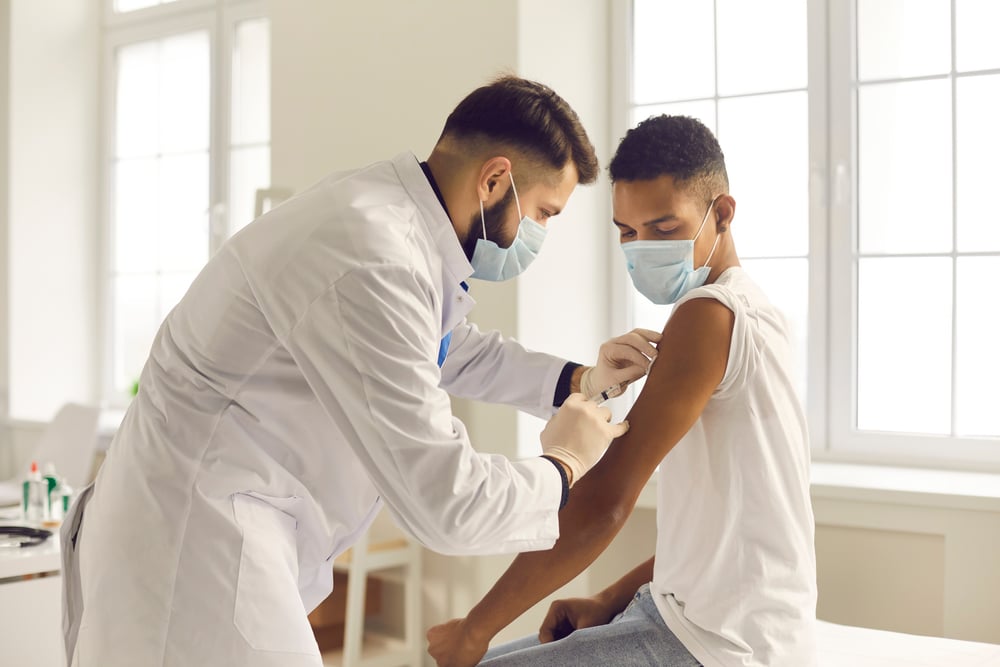 medical professional wears mask as he vaccinates a male masked patient