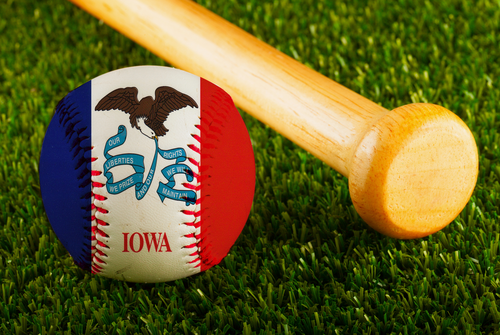 baseball with Iowa flag lies on grass pitch near bat